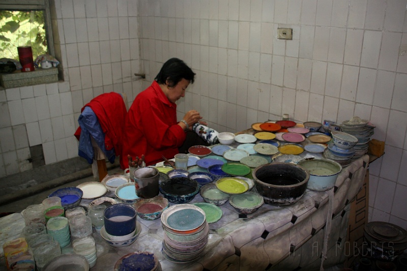 cloisonne1.jpg - In Beijing we went to the Cloisonne factory where they showed us the process of making these beautiful works of art.  Here a woman is loading the enamel pigment into the designs which have been glued onto the vase with copper wire.